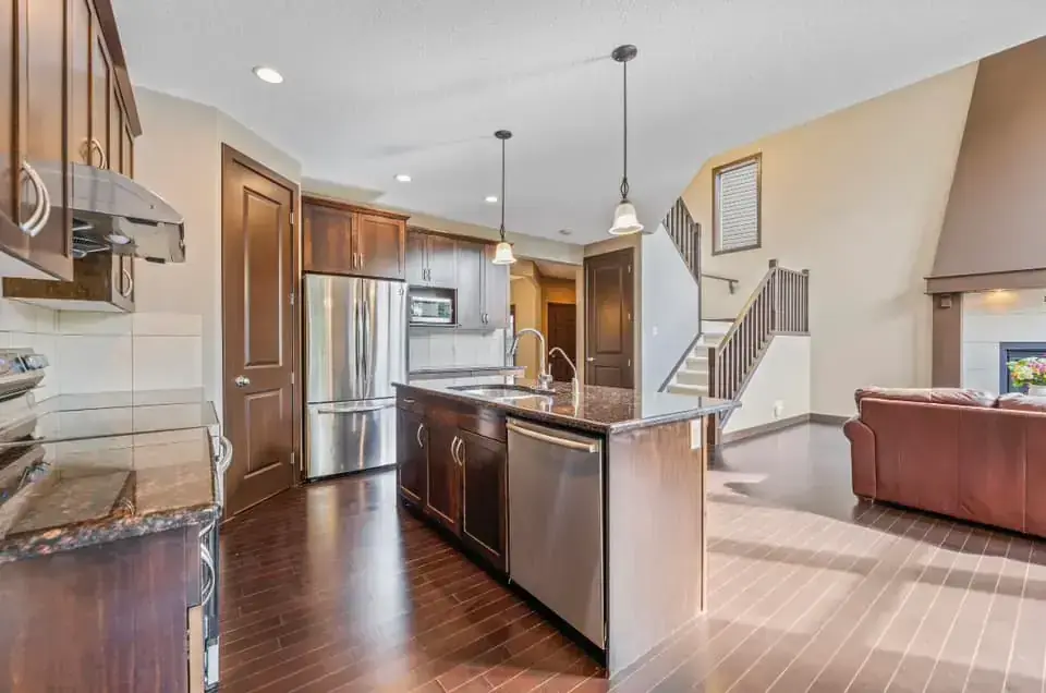 Open-concept kitchen with dark wood cabinetry, granite countertops, island with pendant lights in Calgary