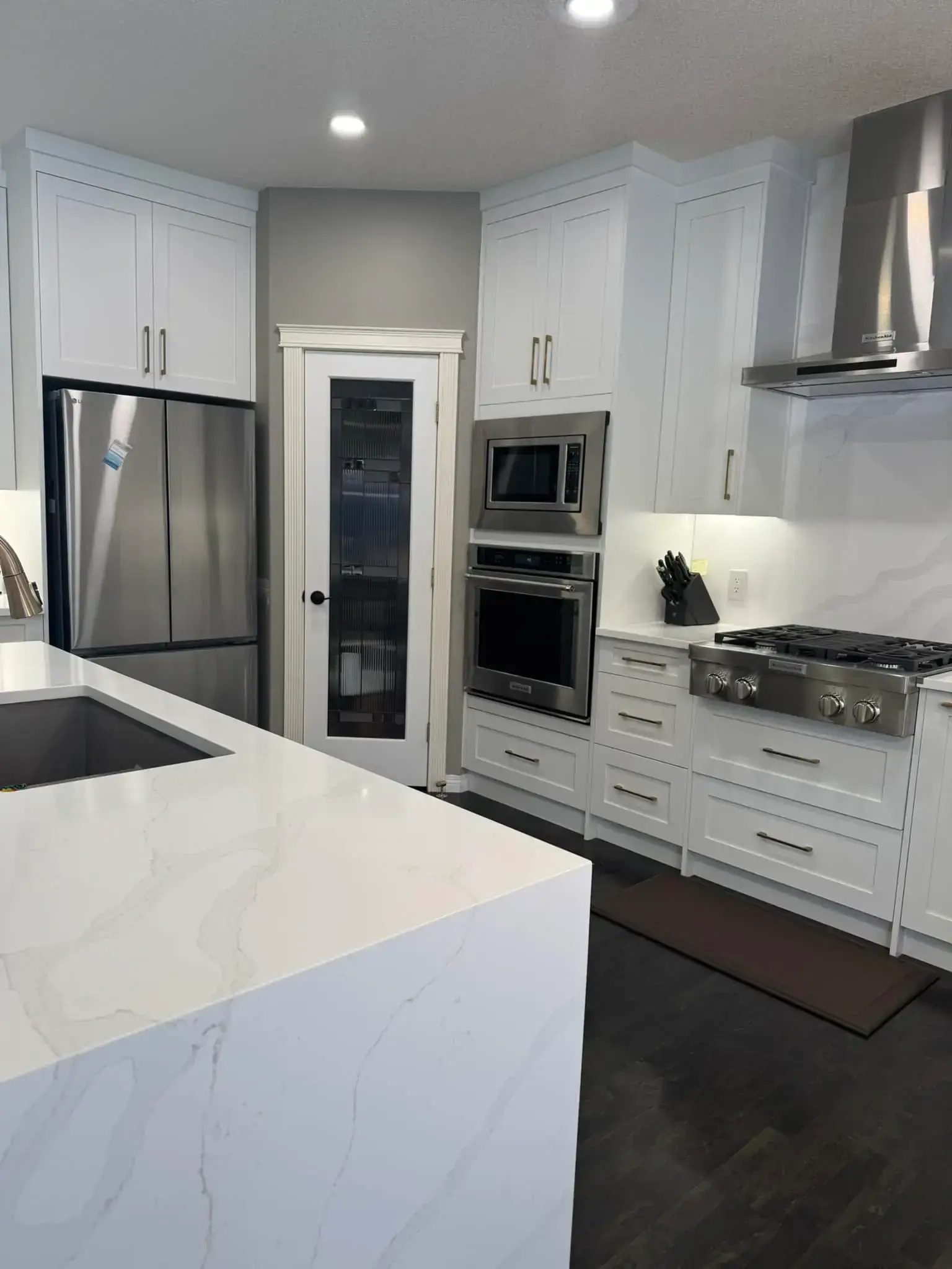 Modern kitchen renovation with white shaker cabinets, quartz countertops, stainless steel appliances, and waterfall island in Calgary